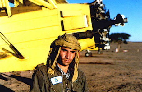 Piloto con turbante junto a un biplano Grumman amarillo en el desierto