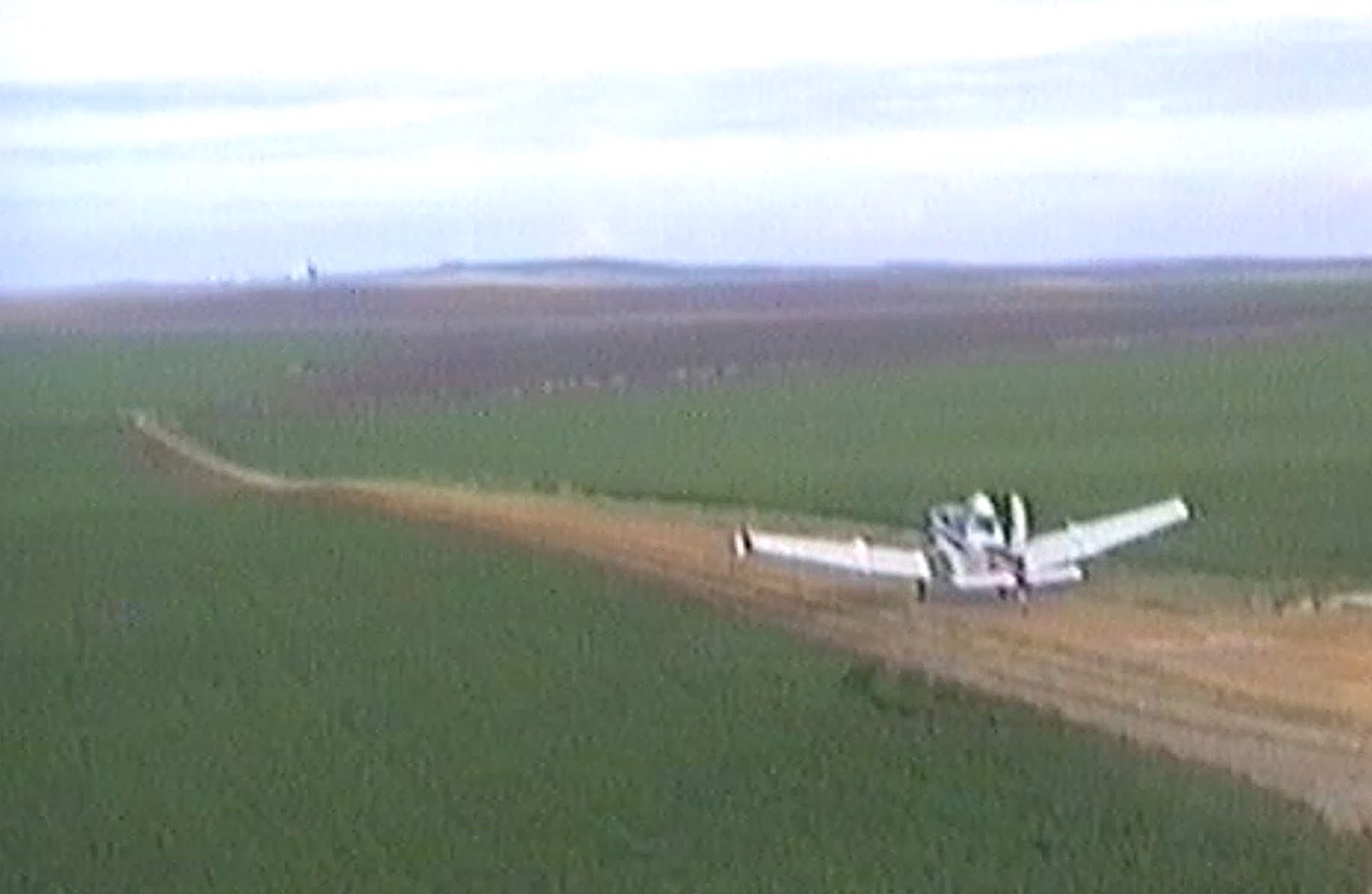 Avioneta de fumigación rodando por un camino de tierra entre campos de trigo verde