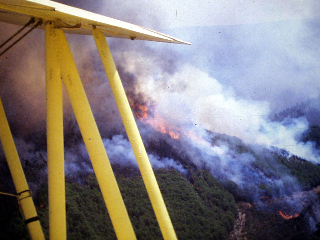 Vista del incendio en la ladera, con llamas y humo, desde la cabina del biplano amarillo
