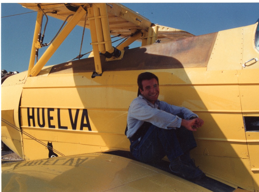 Juan Carlos Gómez Verdugo sentado sobre el biplano amarillo "Gato 5", con el rótulo HUELVA