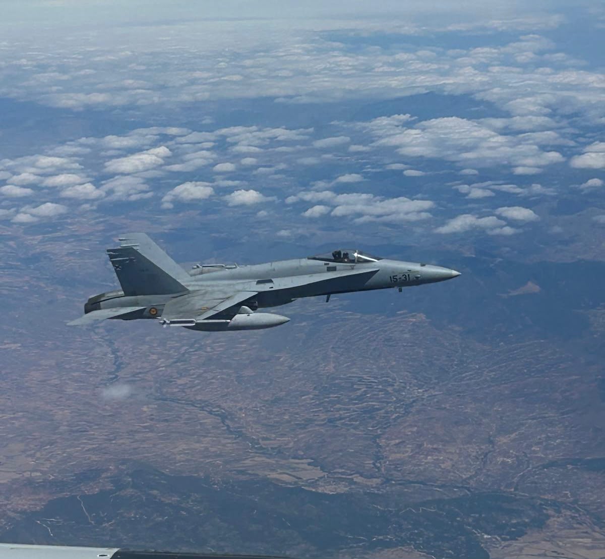 Caza F/A-18 del Ejército del Aire en vuelo sobre un paisaje de montañas y nubes
