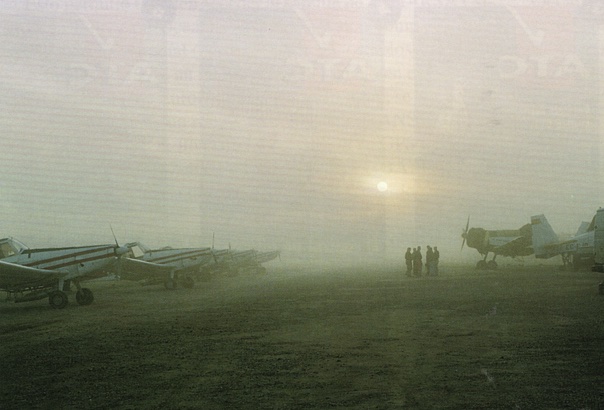 Avionetas aparcadas en la base envueltas en niebla, con los pilotos charlando al amanecer
